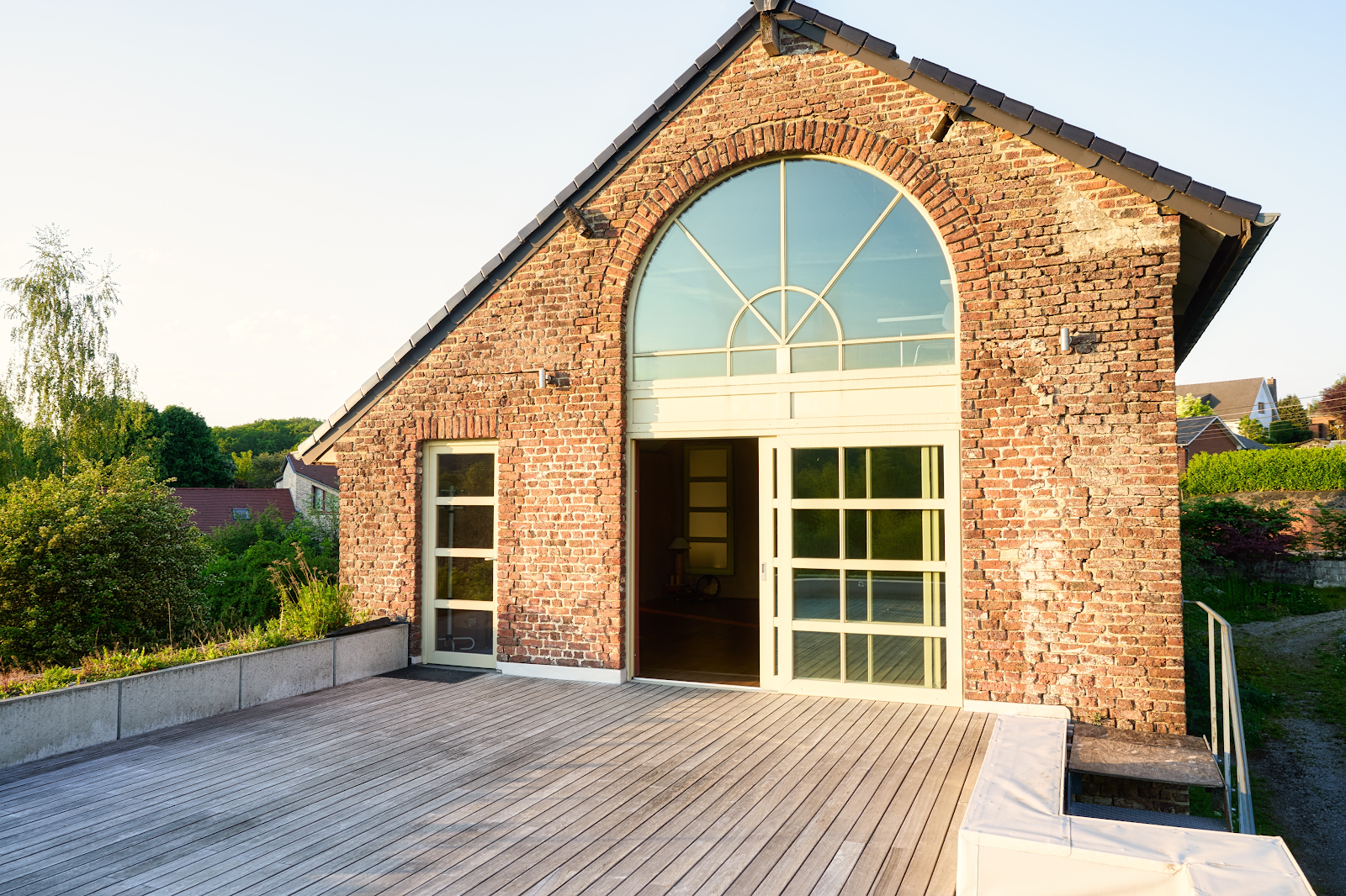 Bâtiment en briques avec une grande fenêtre en demi-cercle et une terrasse en bois